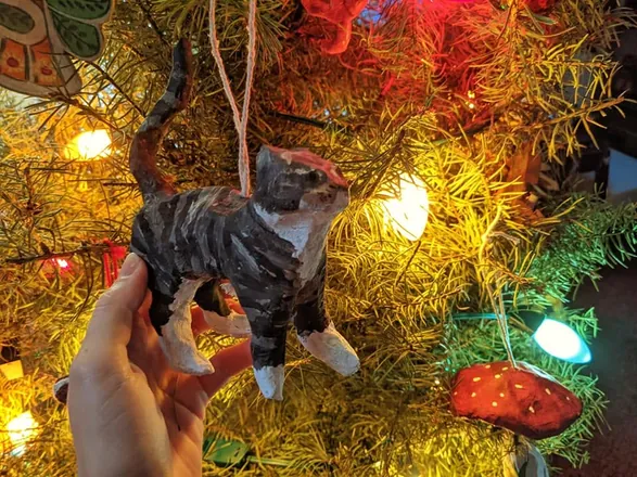A dog ornament held up in front of a Christmas tree