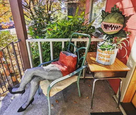 A pair of legs in fishnets and heels on a porch chair, beside a man-eating plant
