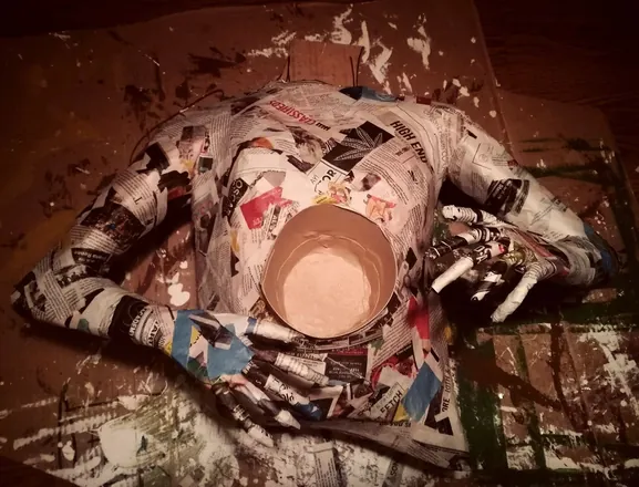 A figure in bare newspaper holding a flower pot, drying on the floor