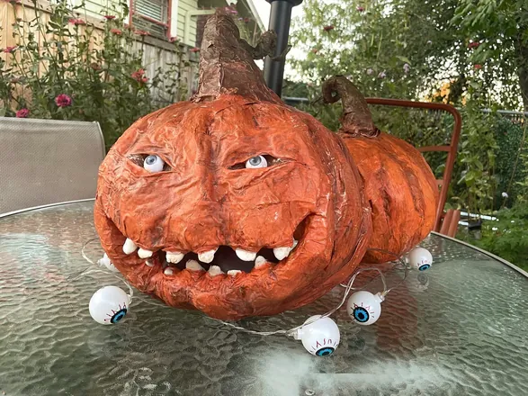 A grinning orange pumpkin with googly eyes on a garden table