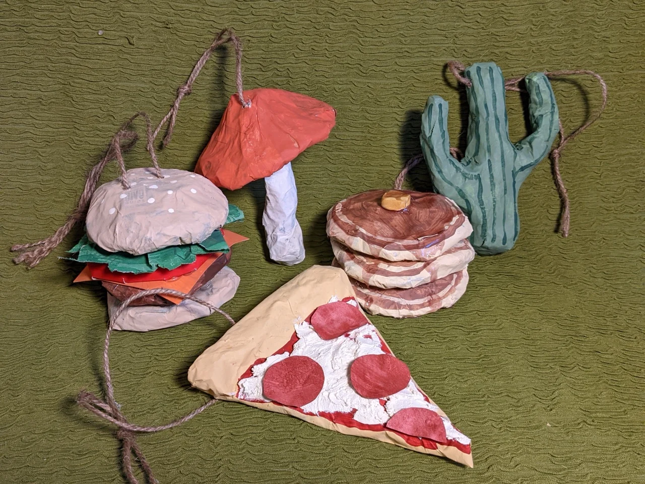 Paper mâché ornaments on string — a burger, a pizza slice, pancakes, a cactus and a mushroom
