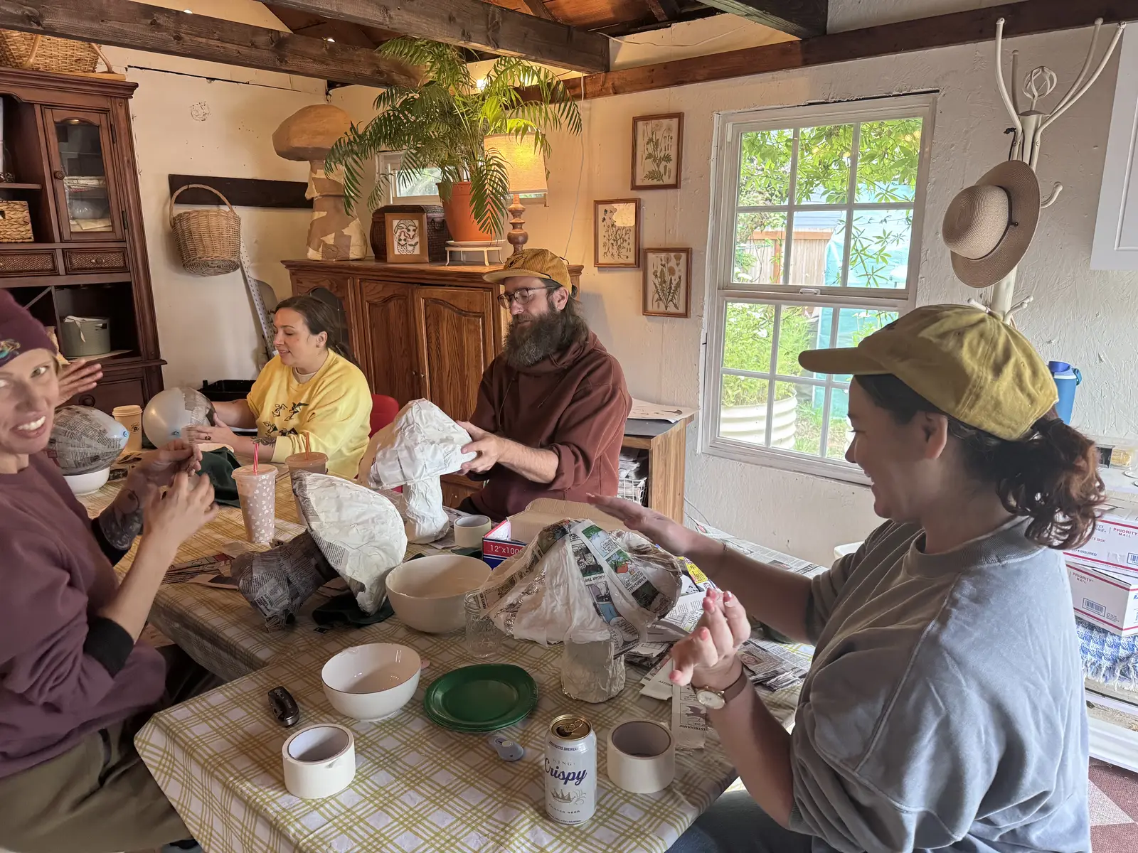 Five people around the studio table, shaping paper mâché and laughing