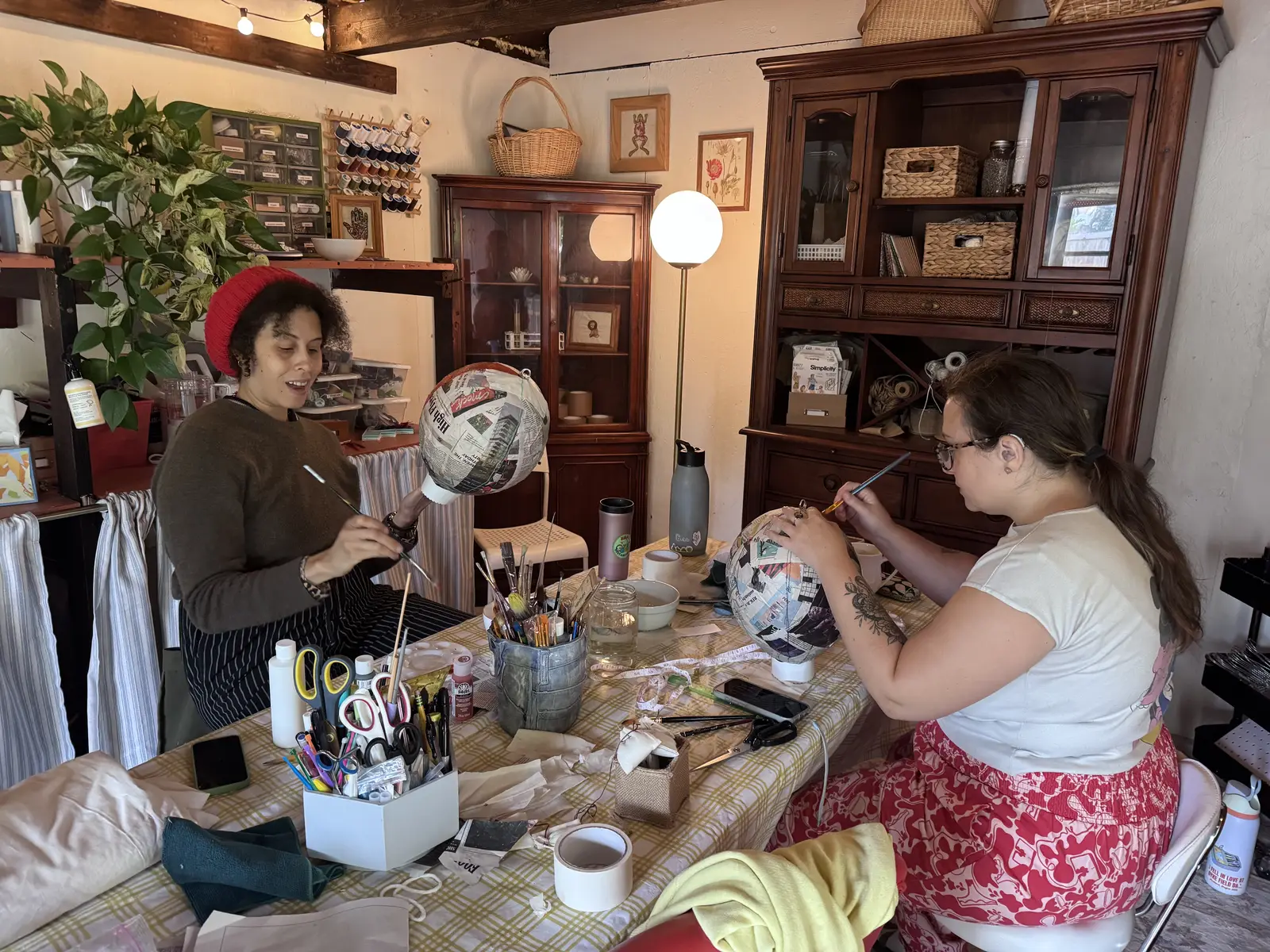 Two people painting their paper mâché balloons at the table